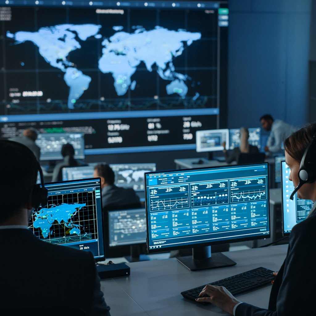 Female analyst looks at screen in a mission control style operations center, surrounded by other employees. Wall display shows global map and charts.